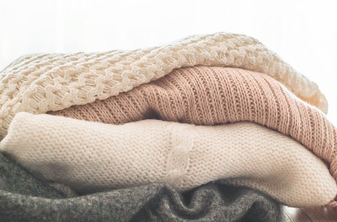 Knitted sweaters from recycled yarn A stack of knitted sweaters in the interior of the living room. The concept of autumn winter comfort.
